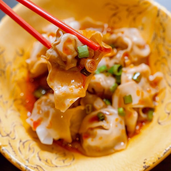 Red chopsticks holding a Reren Ramen dumpling from a yellow bowl, garnished with green onions.