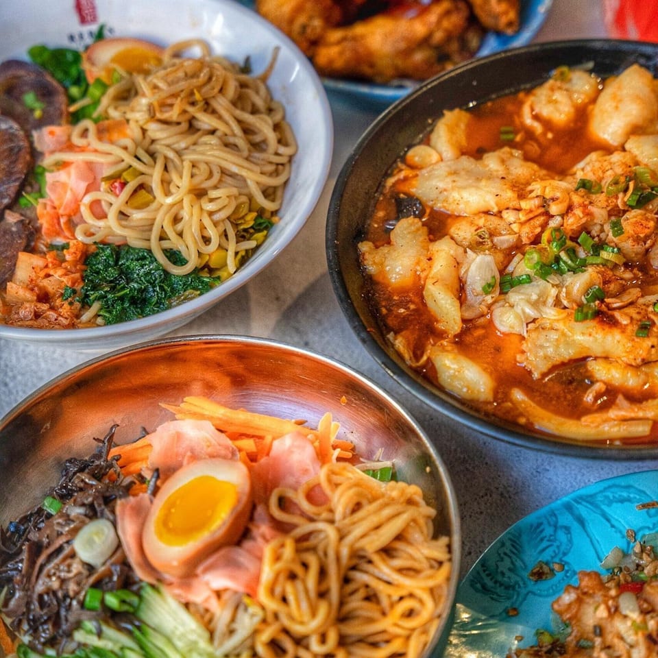 Three bowls of Reren Lamen n Bar ramen and a side dish on a table.