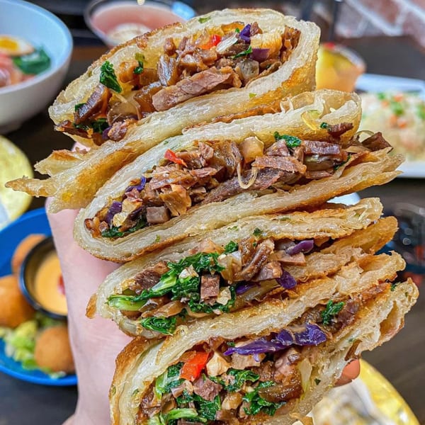 Hand holding stacked crispy scallion pancakes filled with beef, kale, and red cabbage.