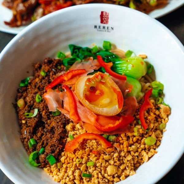 A bowl of Reren Lamen with minced meat, peanuts, bok choy, red peppers, and a soft-boiled egg.